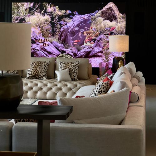 Sala de estar con sofá capitoné, cojines estampados y acuario digital integrado, en casa reformada del Maresme por Prada’s Design.